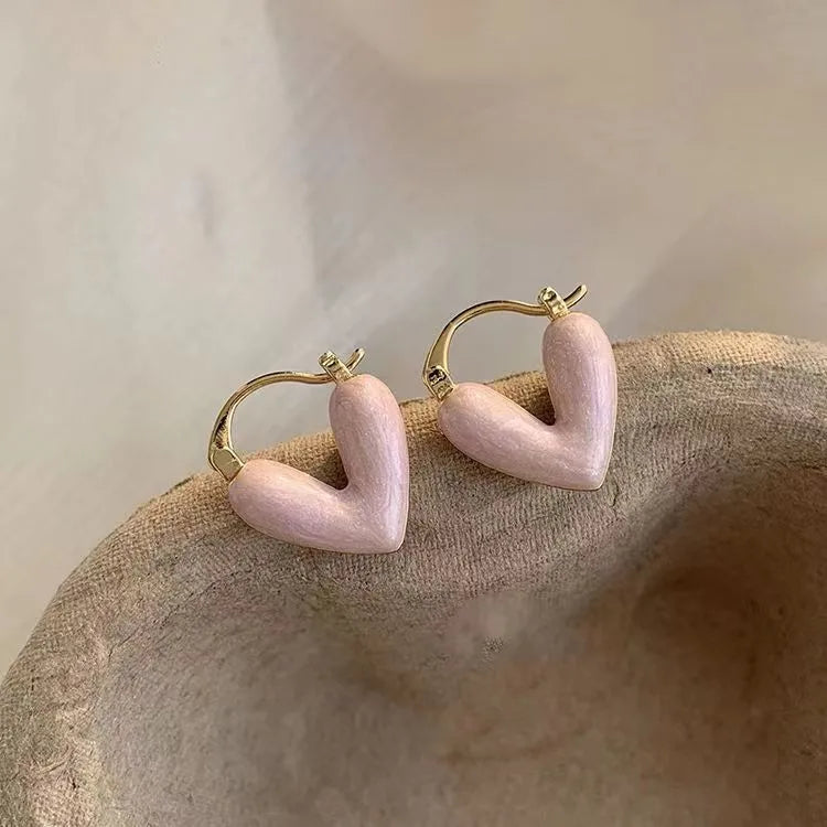 Pink hoop earrings with gold accents on a textured beige surface